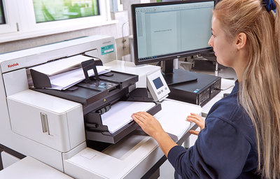 Digitalisierung von Dokumenten – REISSWOLF Scanservice für Unternehmen Mitarbeiterin scannt Papierdokumente mit professionellem Kodak-Dokumentenscanner