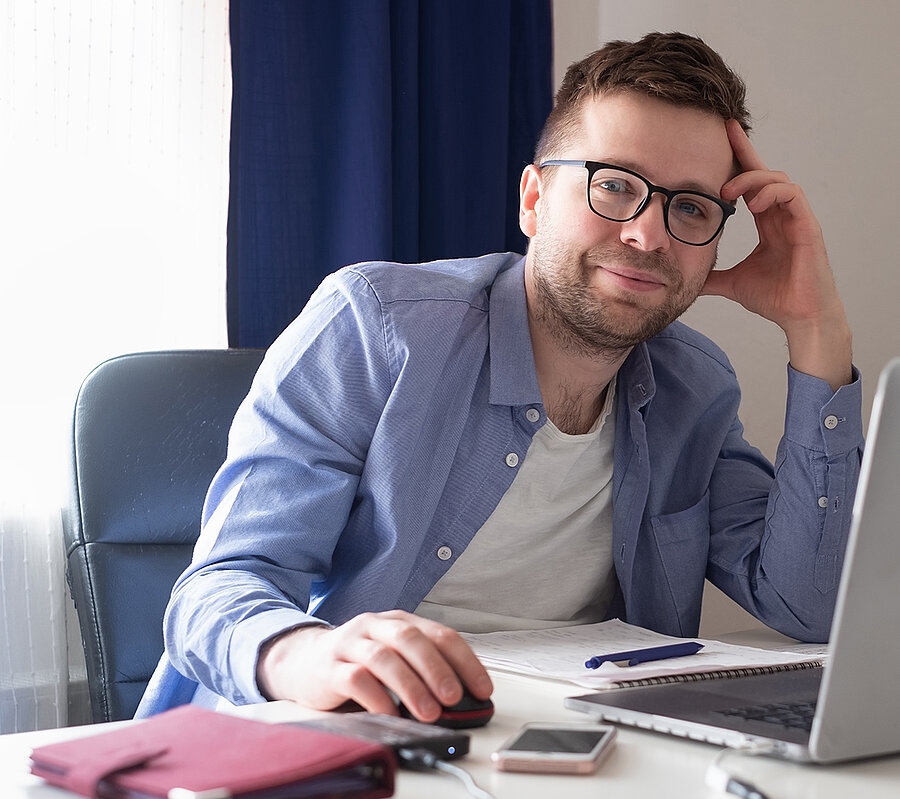 Ein Mann mit Brille sitzt an einem Schreibtisch mit einem Laptop.