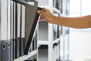 Hand greift einen Ordner aus Regal raus