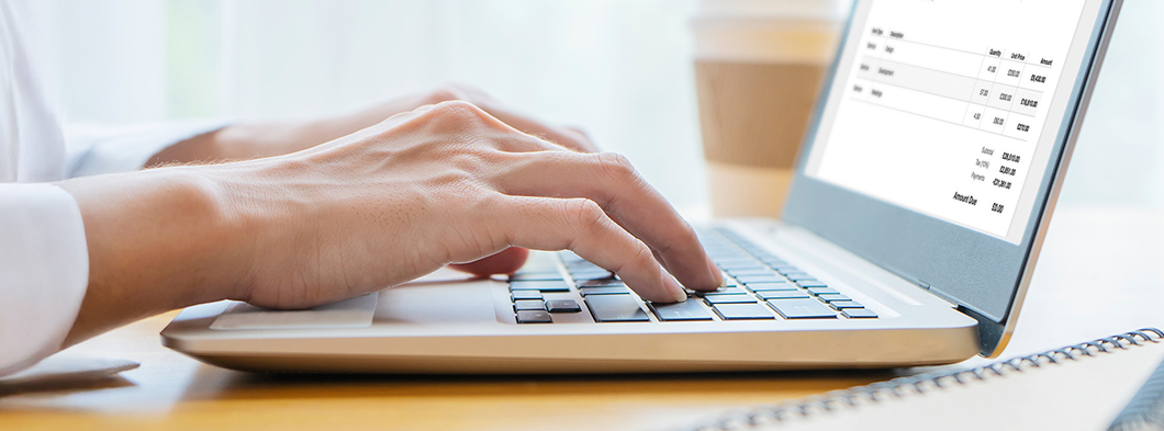 Hände bearbeiten Rechnungen digital am Laptop.