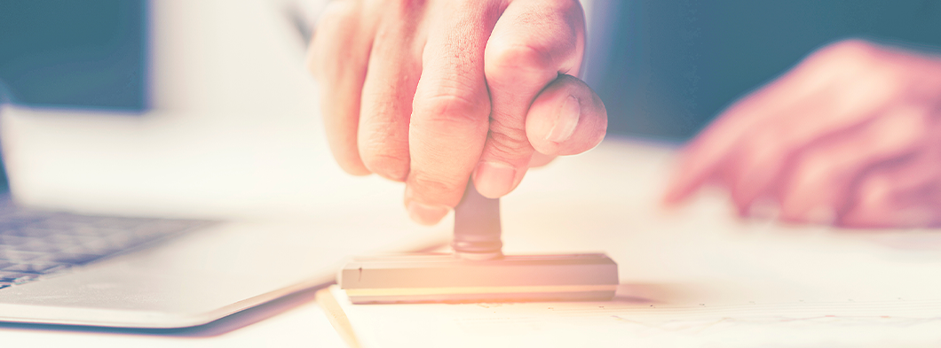Hand setzt einen Stempel auf ein Dokument, symbolisiert Zertifizierung und Audit.