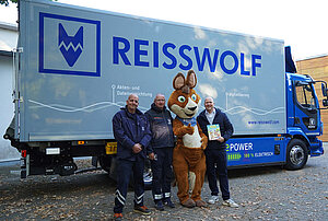 Gruppenfoto des REISSWOLF Teams mit dem Maskottchen Blicki vor einem Presswagen.