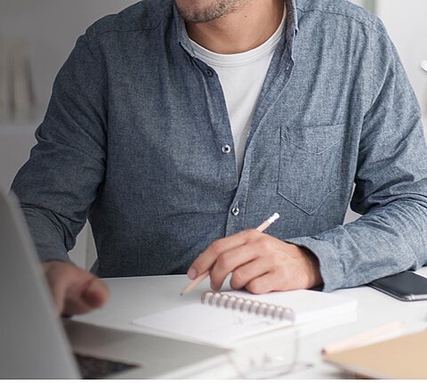 Ein REISSWOLF Kunde sitzt mit einem Block und Stift in der Hand an einem Laptop