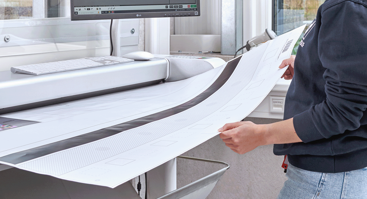 Mitarbeiterin im grauen Pullover scannt großformatige Dokumente mit einem Hochleistungsscanner