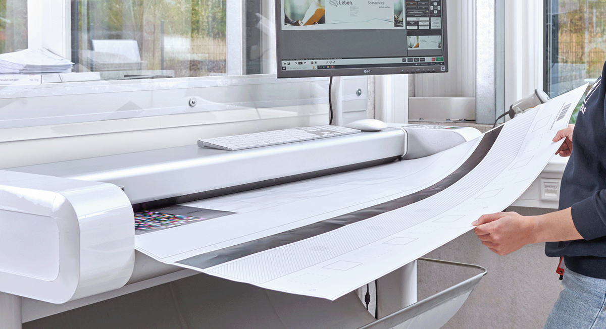 Mitarbeiterin im grauen Pullover scannt großformatige Dokumente mit einem Hochleistungsscanner
