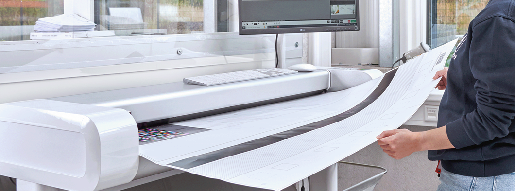 Mitarbeiterin im grauen Pullover scannt großformatige Dokumente mit einem Hochleistungsscanner