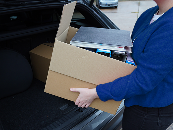 Person hebt einen Karton mit Akten aus einem Kofferraum